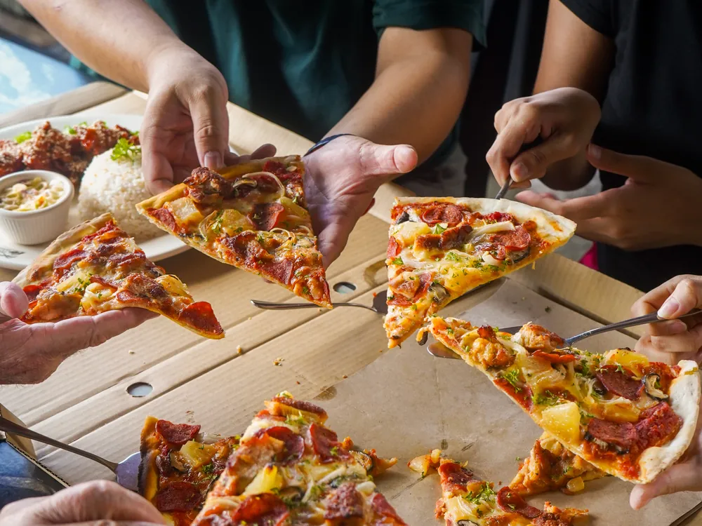 Friends sharing pizza slices from an open box at a Big Coconut table